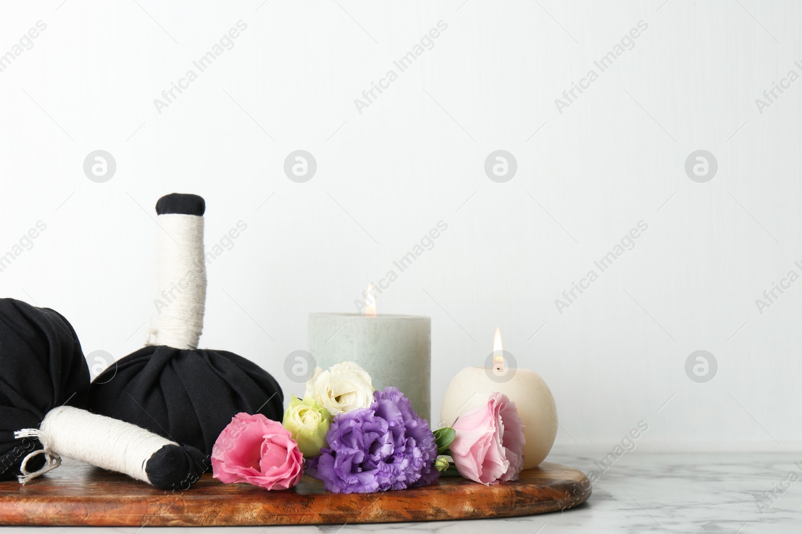 Photo of Spa treatment. Massage bags, burning candles and beautiful flowers on white marble table, space for text