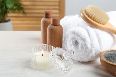 Photo of Spa treatment. Towel, brush, cosmetic products and candle on white table, space for text