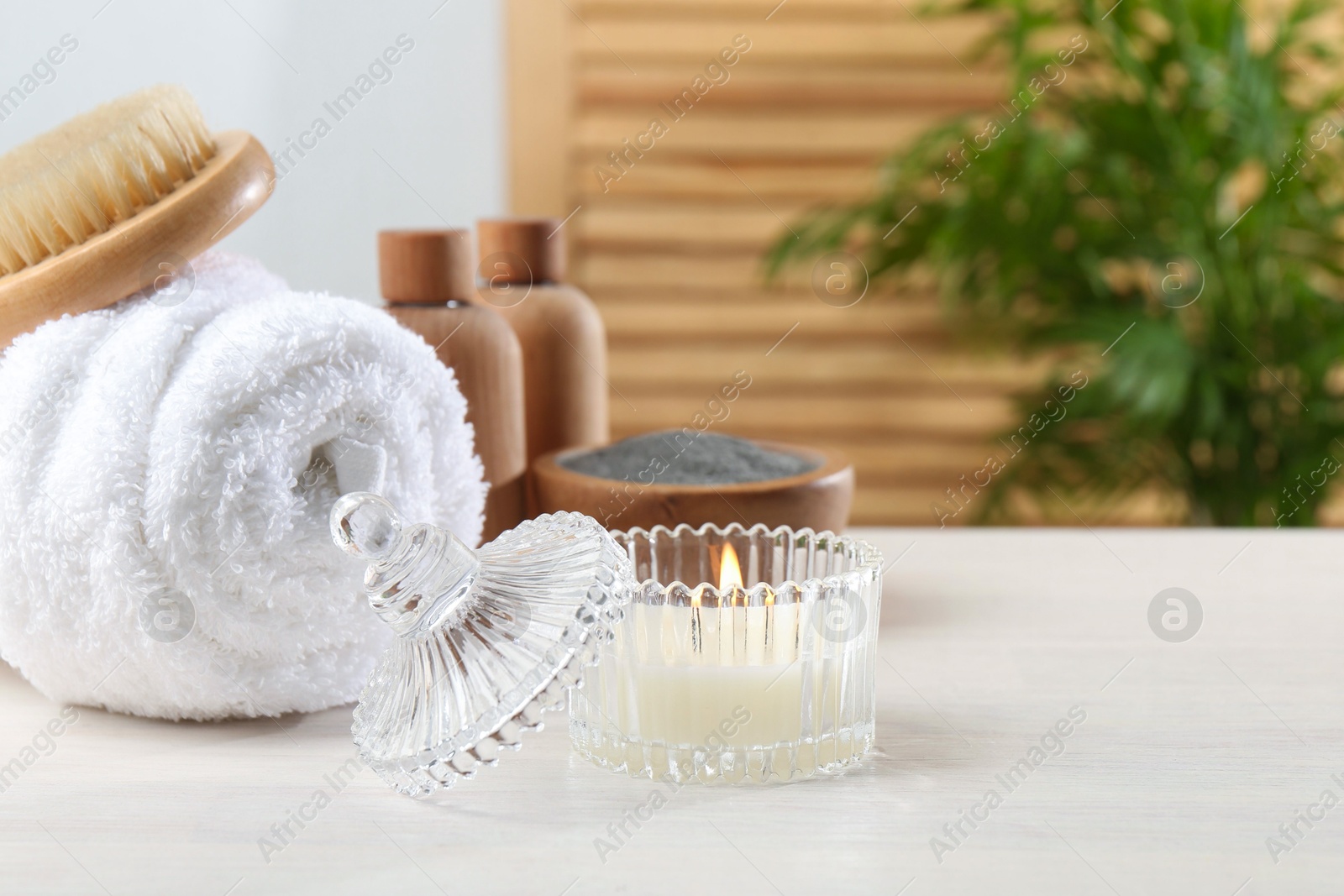 Photo of Spa treatment. Towel, brush, cosmetic products and candle on white table, space for text