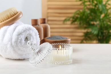 Photo of Spa treatment. Towel, brush, cosmetic products and candle on white table, space for text