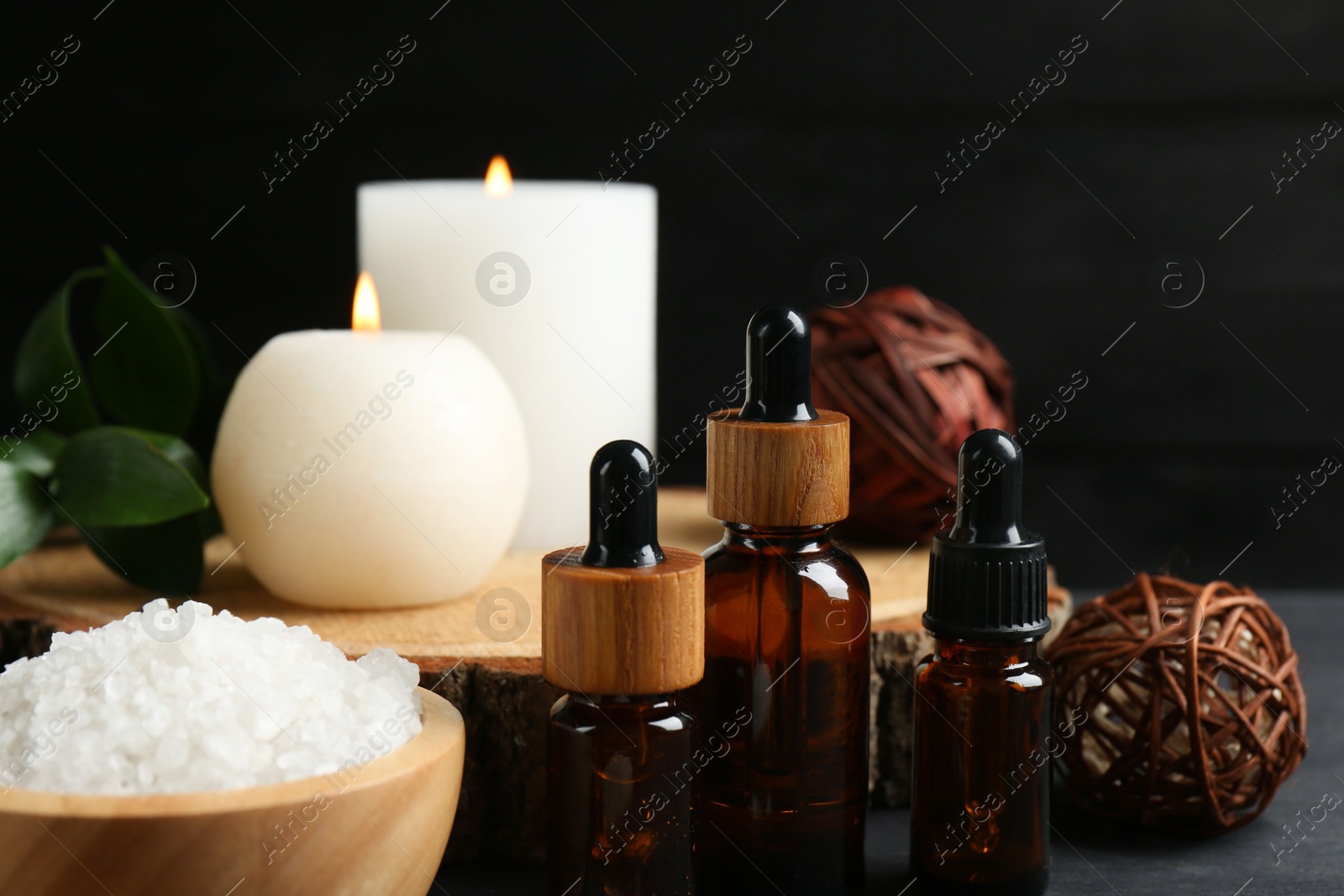 Photo of Composition with cosmetic products and candles for spa treatment on black table, closeup