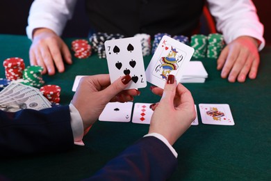 Photo of Professional croupier and gambler at table with playing cards and casino chips, closeup