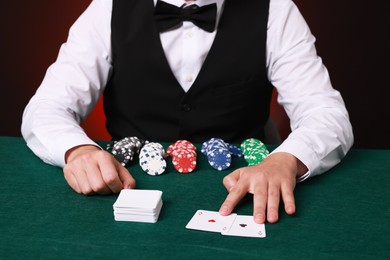 Photo of Professional croupier with playing cards at gambling table, closeup