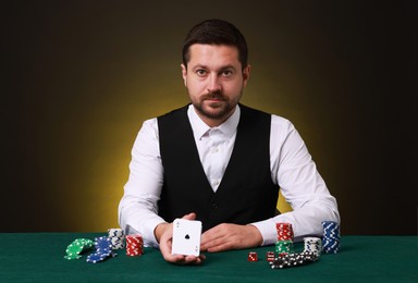 Photo of Professional croupier with playing cards at gambling table against dark yellow background