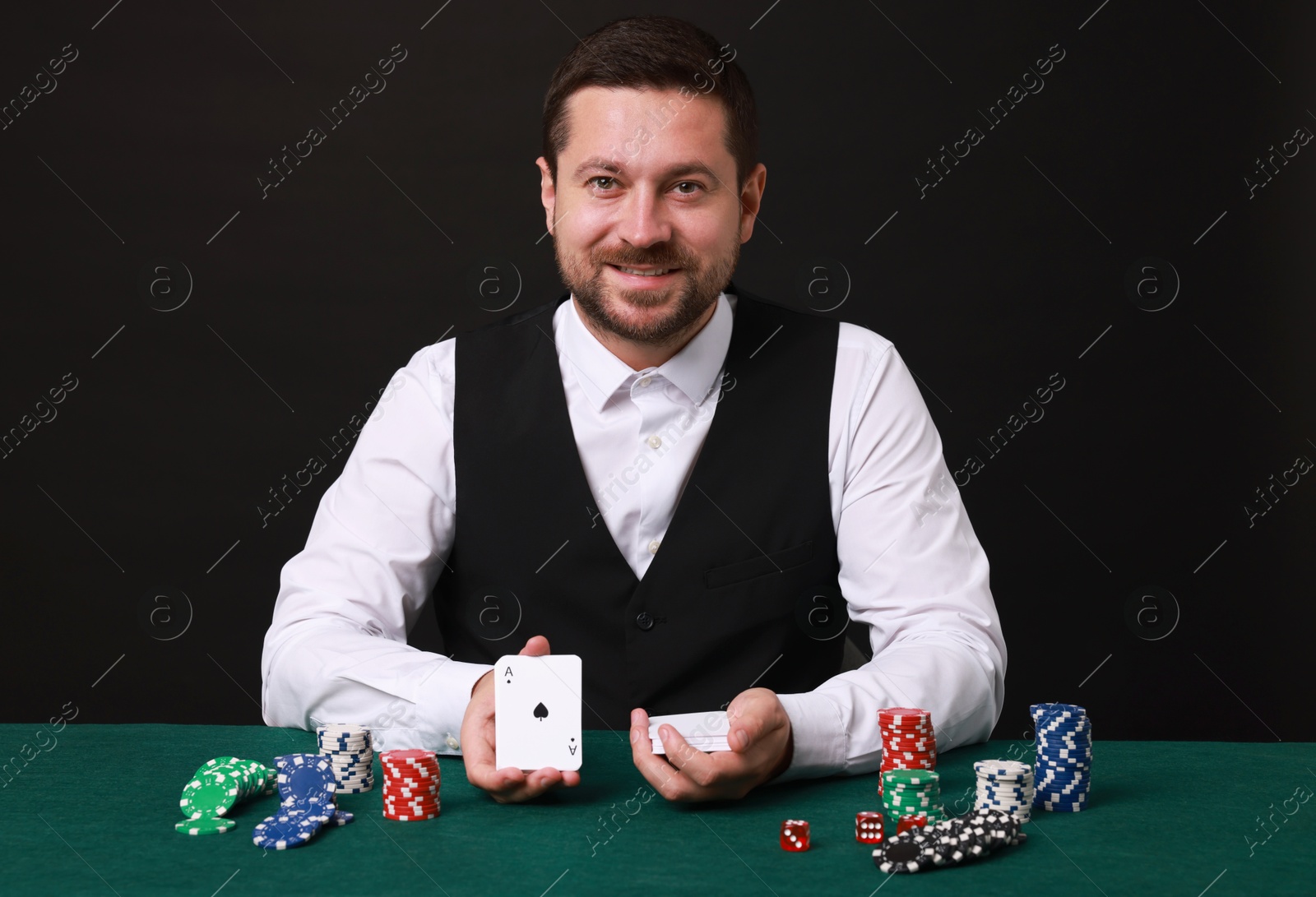 Photo of Professional croupier with playing cards at gambling table against black background