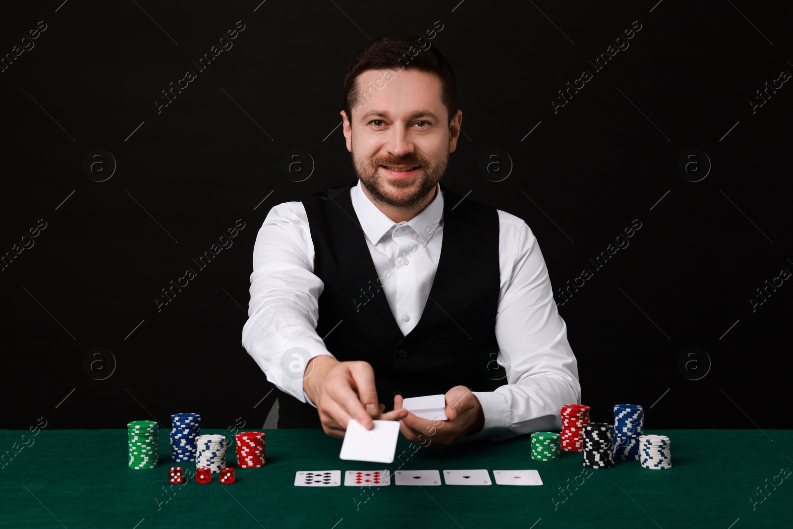 Photo of Professional croupier with playing cards at gambling table against black background