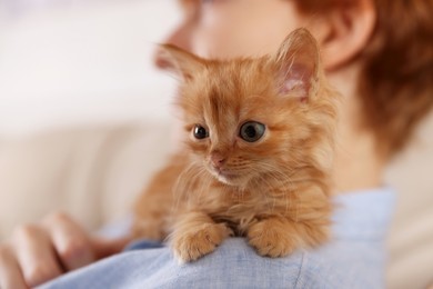 Photo of Teenage boy with cute ginger kitten indoors, closeup