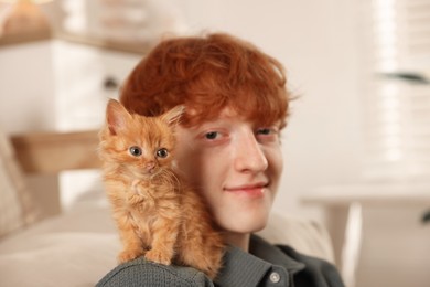 Photo of Redhead teenage boy with cute ginger kitten indoors, selective focus