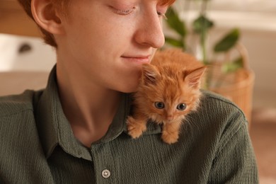 Photo of Teenage boy with cute ginger kitten indoors, closeup