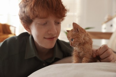 Photo of Redhead teenage boy with cute ginger kitten on sofa indoors