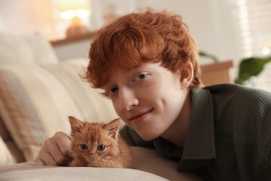 Photo of Redhead teenage boy with cute ginger kitten on sofa indoors