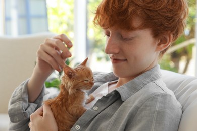 Photo of Redhead teenage boy with cute ginger kitten indoors