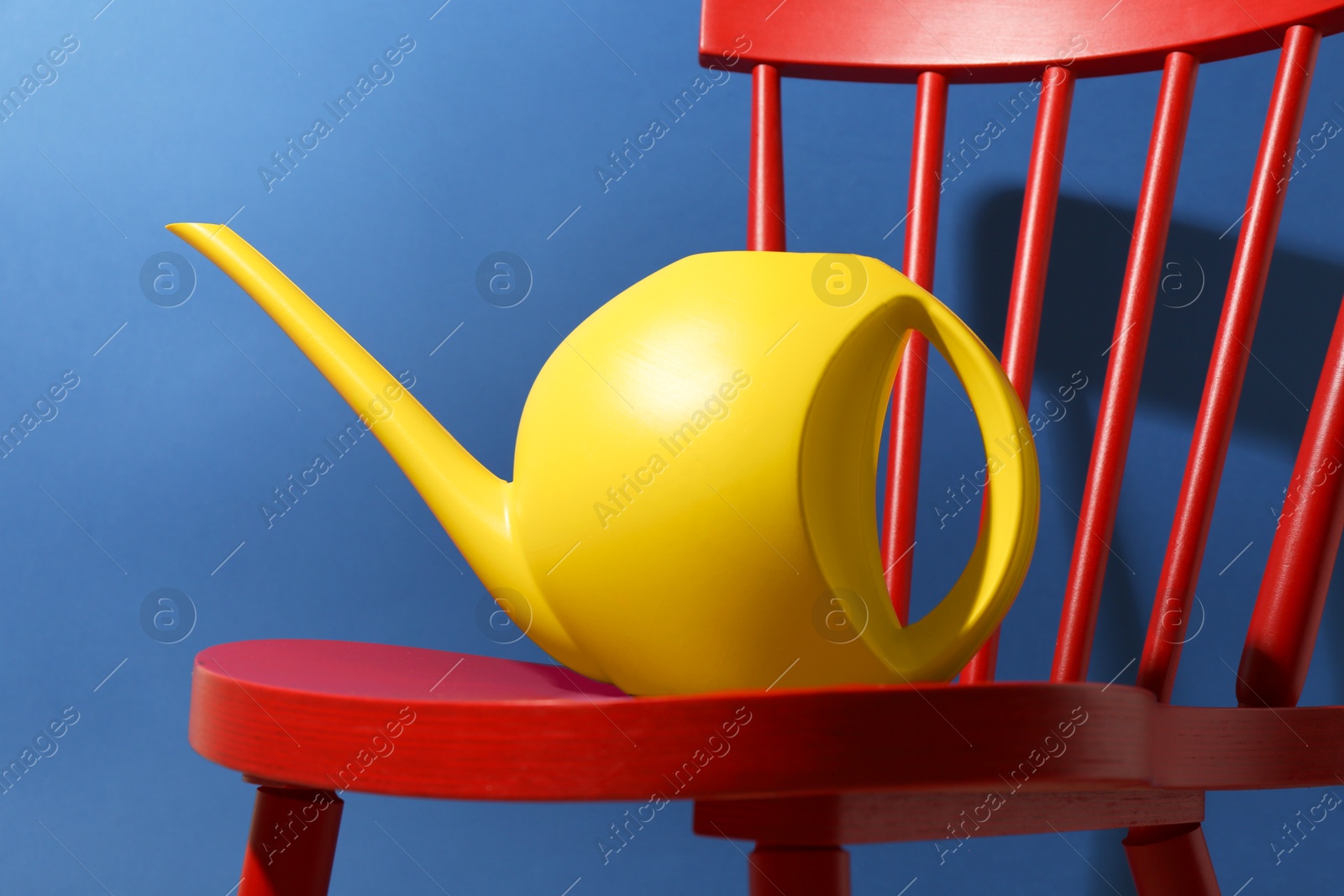 Photo of Yellow plastic watering can on chair against blue background