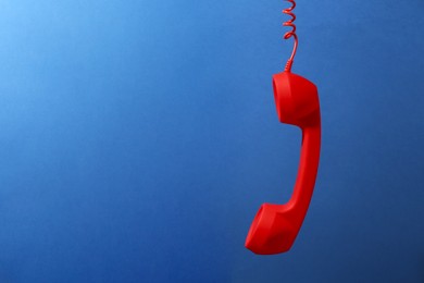 Photo of Red corded telephone handset on blue background. Space for text