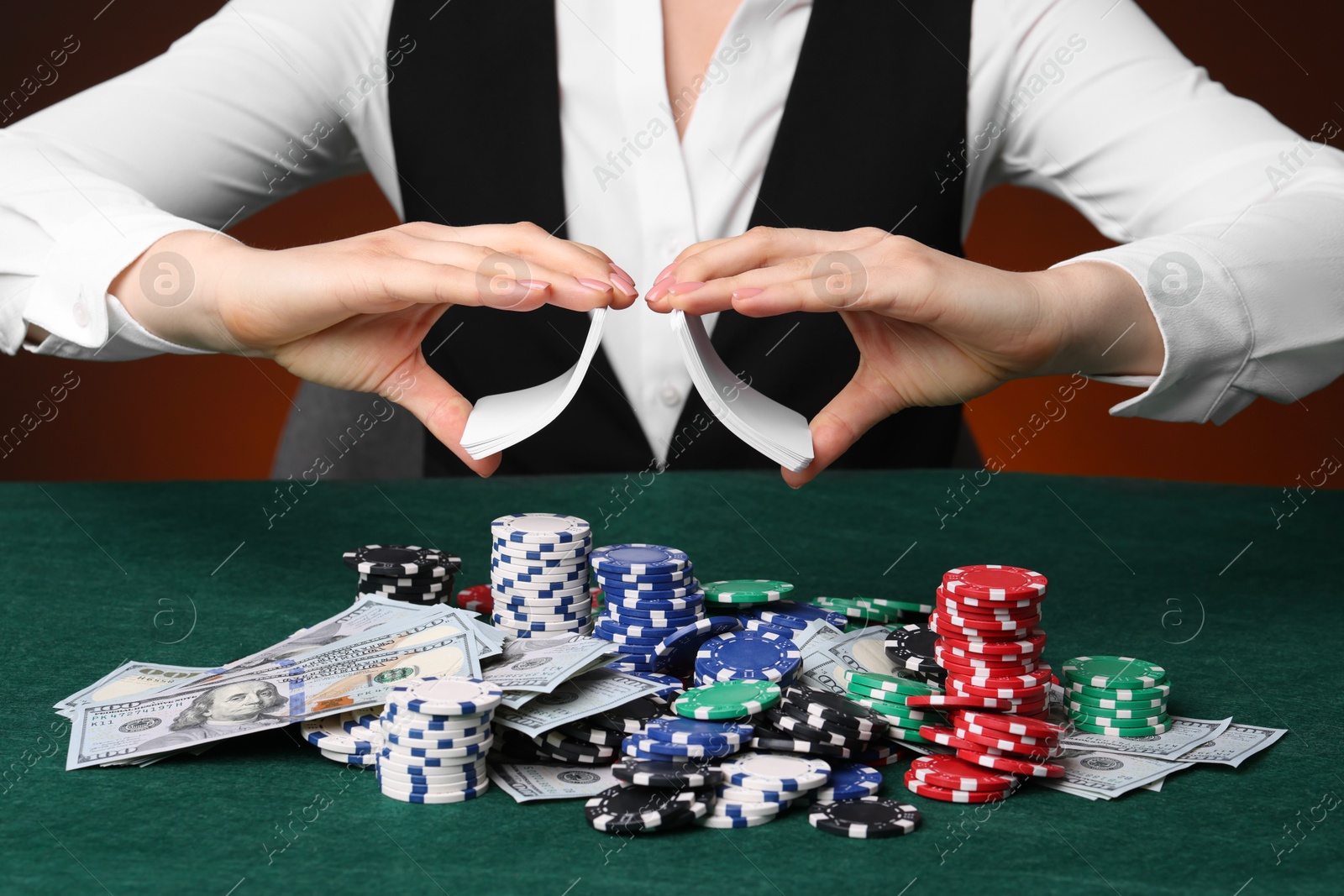 Photo of Professional croupier with chips shuffling playing cards at gambling table on color background, closeup