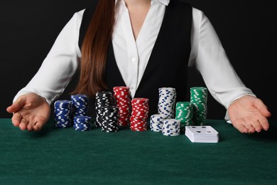 Photo of Professional croupier with casino chips and playing cards at gambling table, closeup