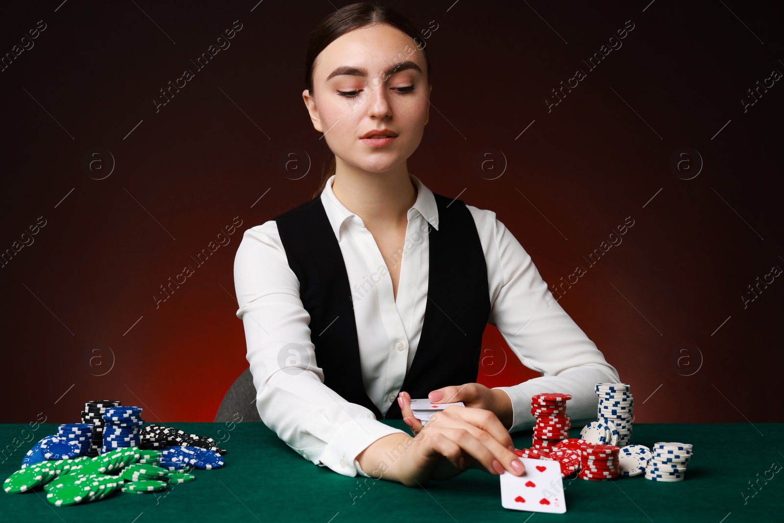 Photo of Professional croupier with casino chips and playing cards at gambling table on color background