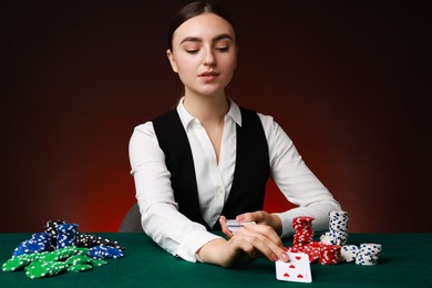 Photo of Professional croupier with casino chips and playing cards at gambling table on color background