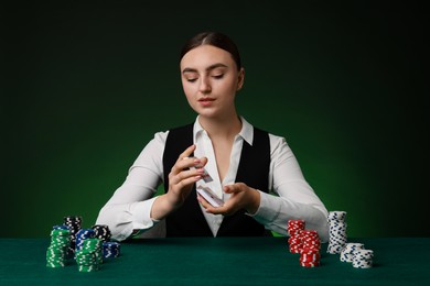 Photo of Professional croupier with chips shuffling playing cards at gambling table on color background