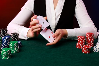 Photo of Professional croupier with chips shuffling playing cards at gambling table on color background, closeup