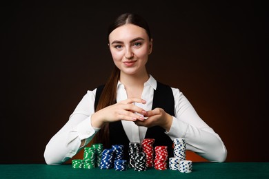 Photo of Professional croupier with casino chips and playing cards at gambling table on color background