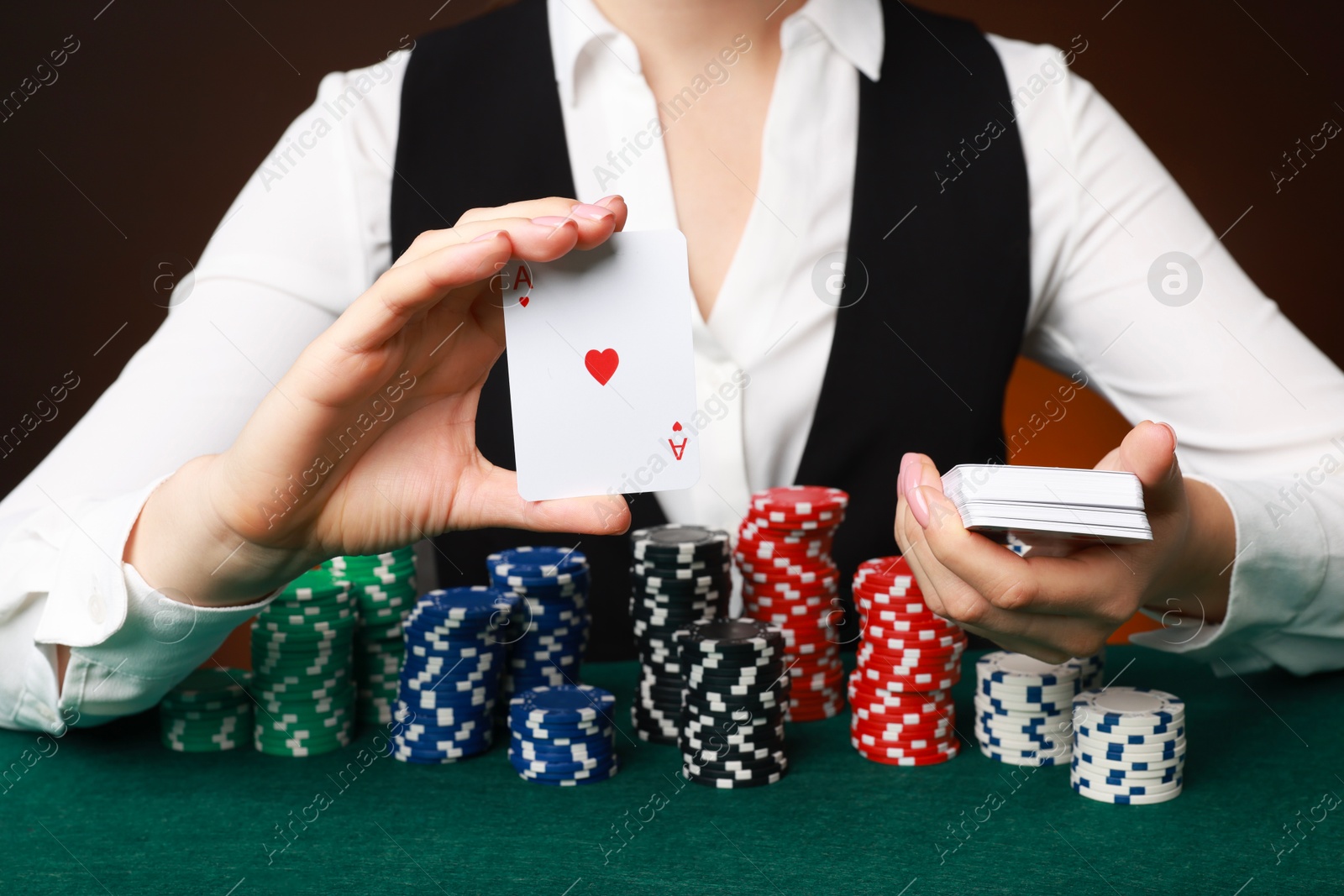 Photo of Professional croupier with casino chips and playing cards at gambling table on color background, closeup