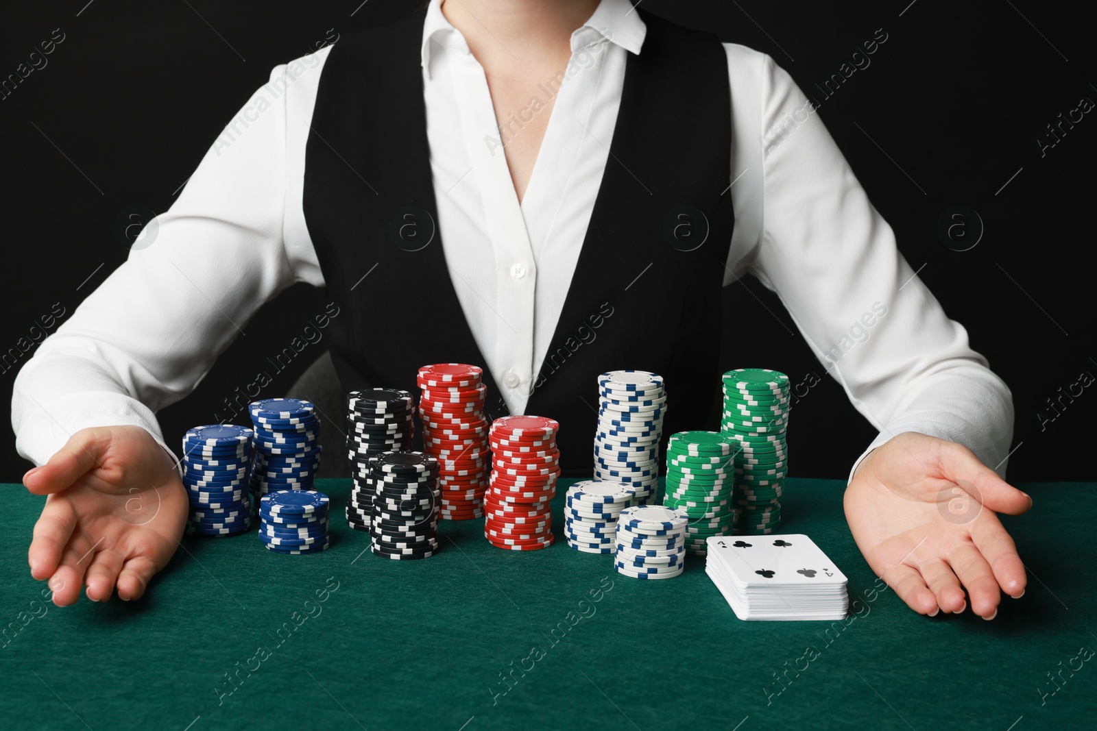 Photo of Professional croupier with casino chips and playing cards at gambling table on black background, closeup