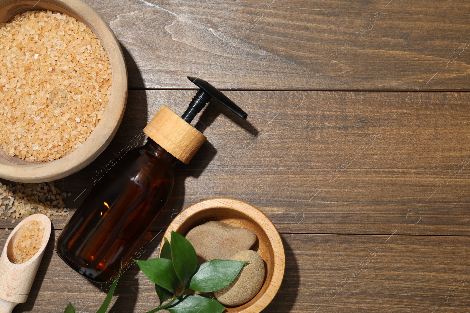 Photo of Spa composition with sea salt, bottle of cosmetic product and leaves on wooden table, flat lay. Space for text