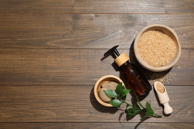 Photo of Spa composition with sea salt, bottle of cosmetic product and leaves on wooden table, flat lay. Space for text