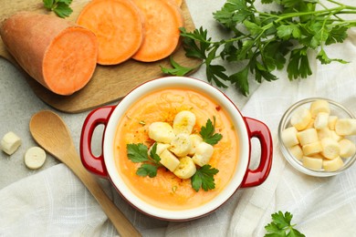 Photo of Delicious sweet potato soup with croutons and fresh ingredients on light textured table, flat lay