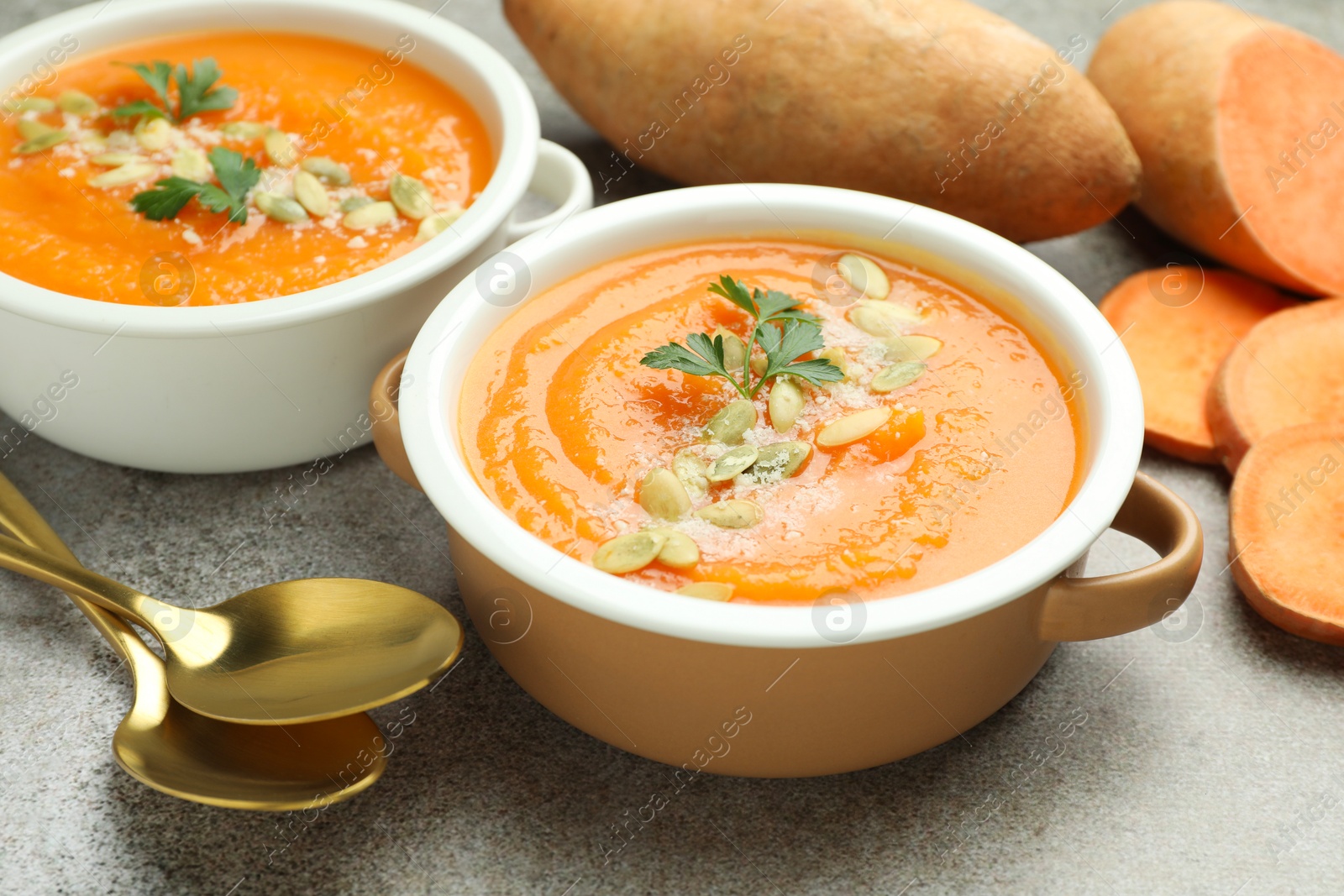 Delicious sweet potato soup with pumpkin seeds in bowls and fresh vegetables on grey textured table, closeup Photo of Delicious sweet potato soup with pumpkin seeds in bowls and fresh vegetables on grey textured table, closeup