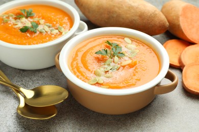 Photo of Delicious sweet potato soup with pumpkin seeds in bowls and fresh vegetables on grey textured table, closeup
