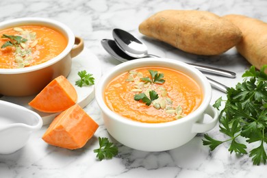 Photo of Delicious sweet potato soup with pumpkin seeds in bowls served on white marble table