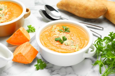 Photo of Delicious sweet potato soup with pumpkin seeds in bowls served on white marble table