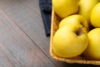 Fresh yellow apples in wicker basket on wooden table, closeup. Space for text