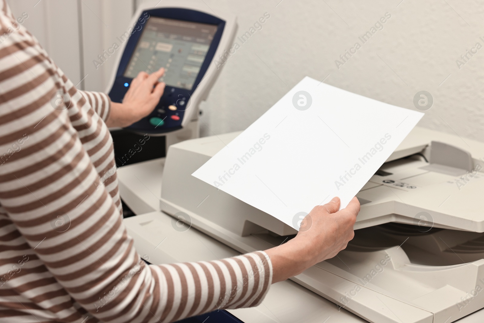 Photo of Woman with paper sheet using modern printer indoors, closeup. Printing house