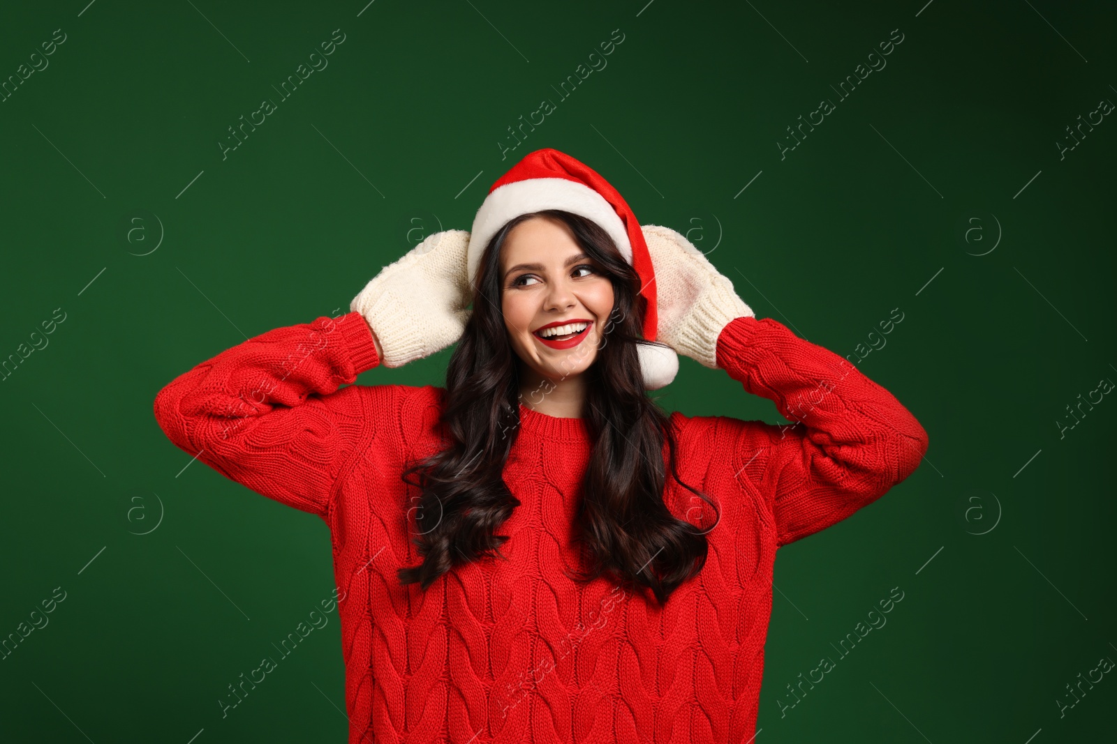 Photo of Attractive woman in Santa hat, sweater and mittens on green background. Christmas celebration