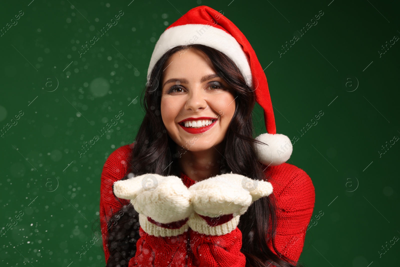 Photo of Attractive woman in Santa hat blowing snow off hands on green background. Christmas celebration