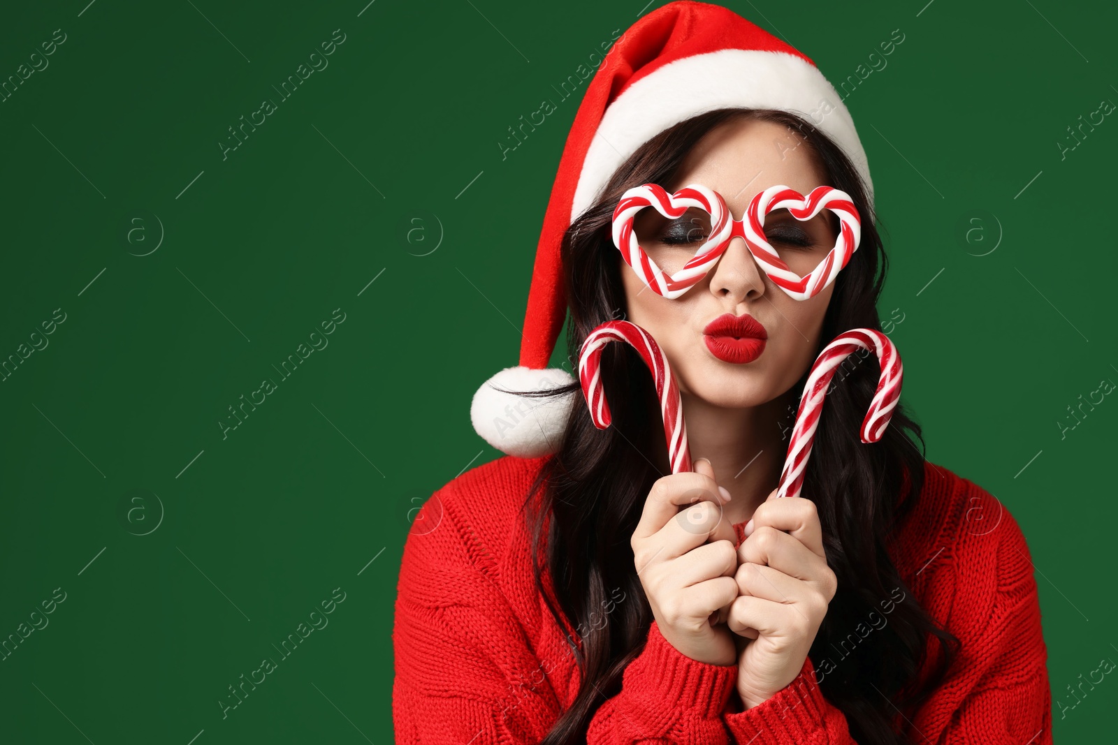 Photo of Beautiful woman in Santa hat and party glasses with candy canes on green background., space for text Christmas celebration