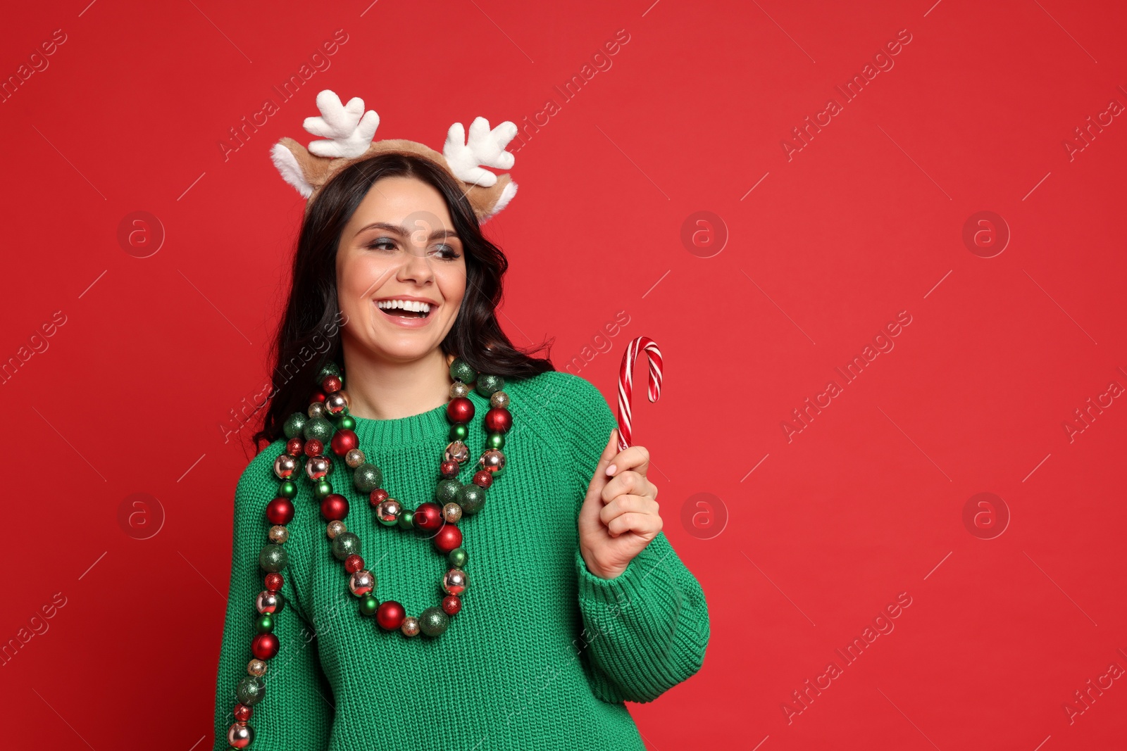 Photo of Beautiful woman with Christmas accessories and candy cane on red background, space for text