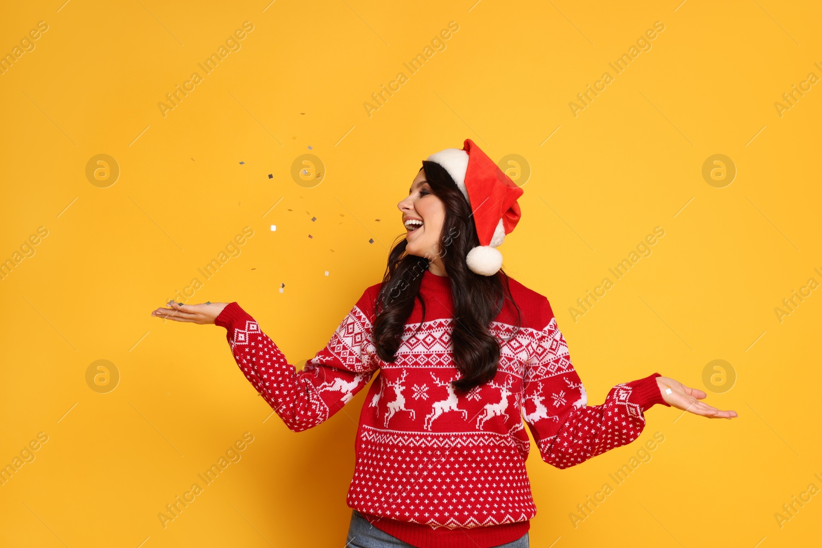 Photo of Beautiful woman in Santa hat and Christmas sweater with confetti on yellow background