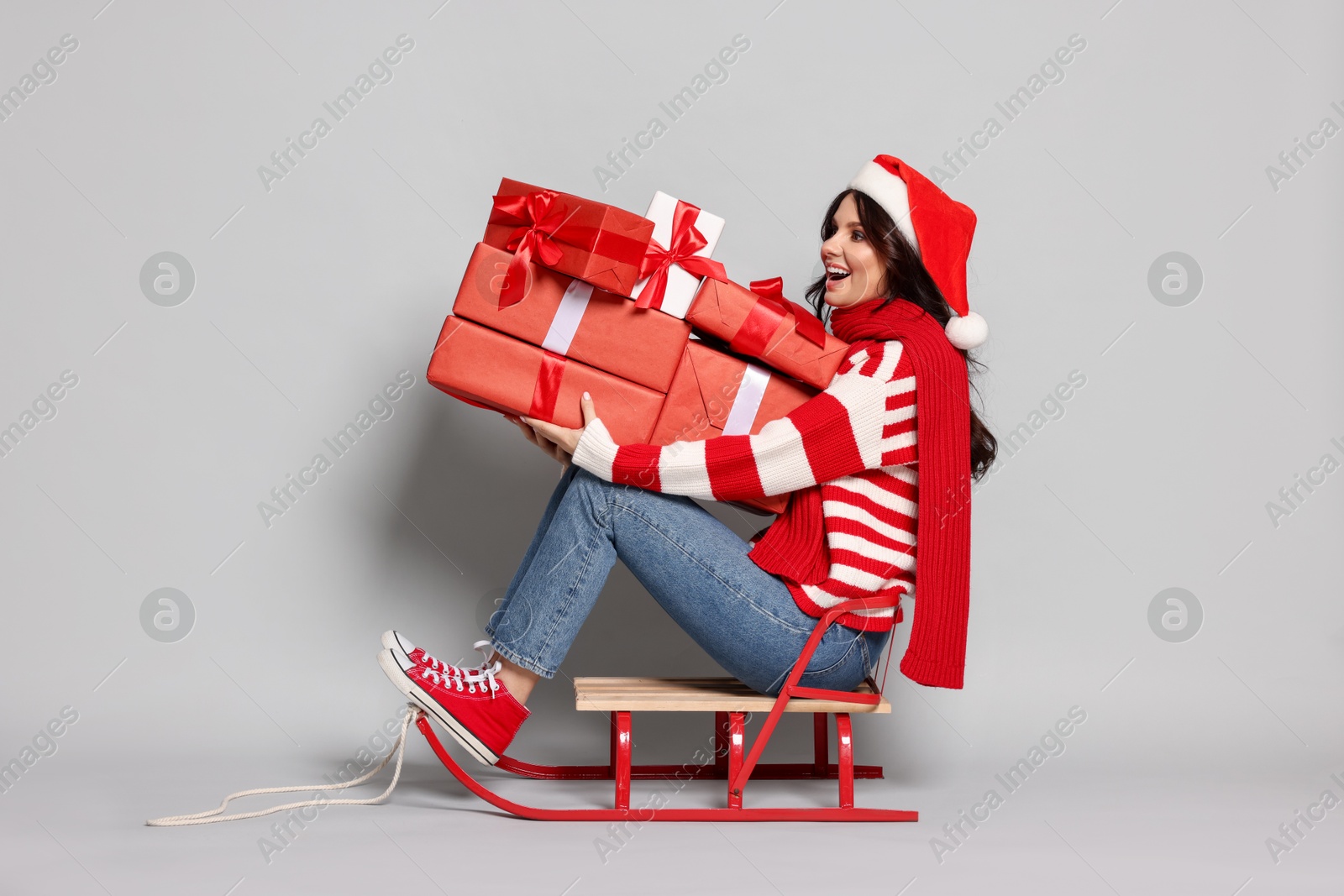 Photo of Woman with Christmas gifts on sledge against light grey background