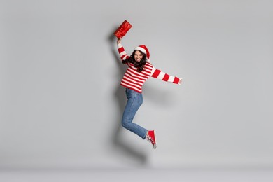 Photo of Woman with Christmas gift jumping on light grey background