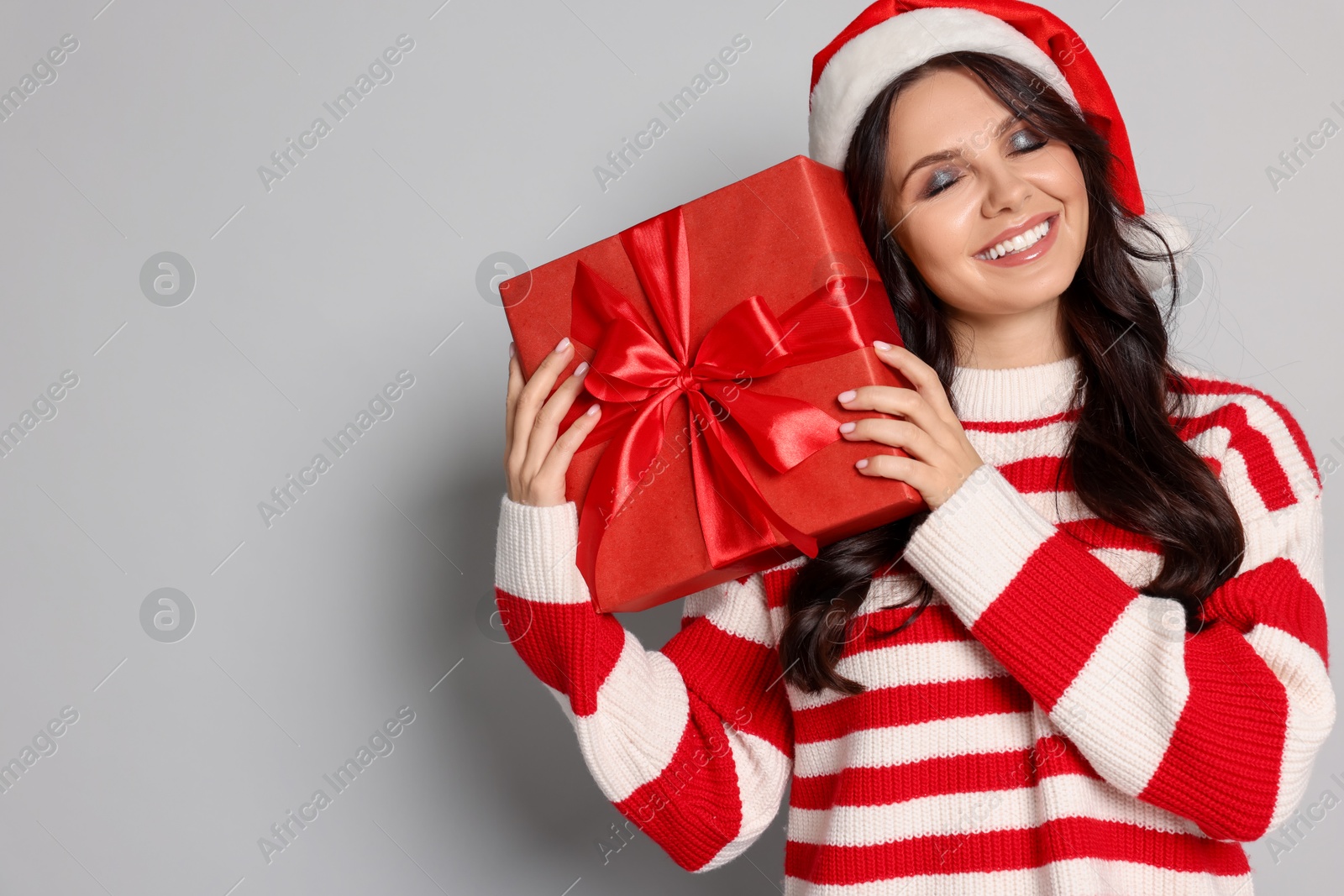 Photo of Woman in Santa hat with Christmas gift on light grey background, space for text