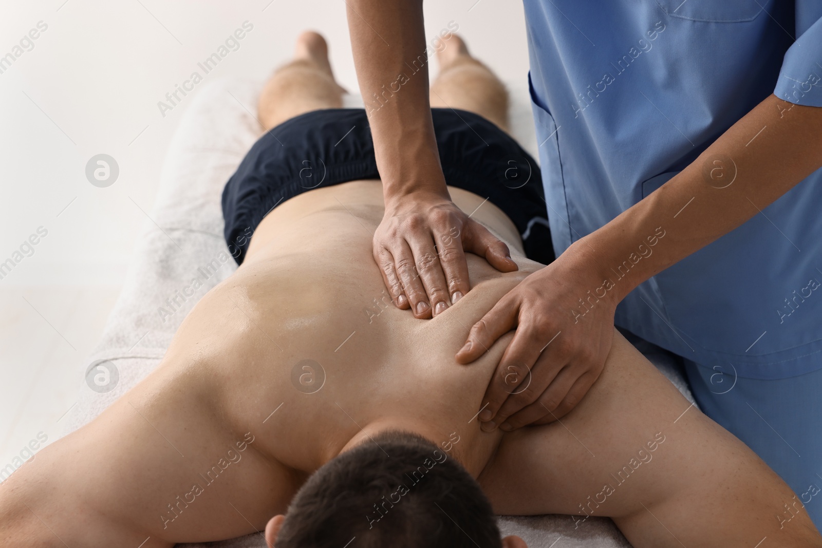 Photo of Professional physiotherapist doing shoulder massage for his client indoors, closeup