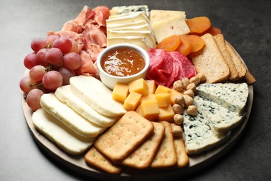 Photo of Different types of cut cheese and other snacks on grey textured table, closeup