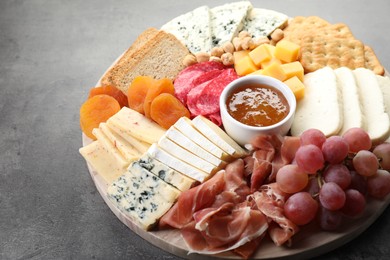 Photo of Different types of cut cheese and other snacks on grey textured table, closeup