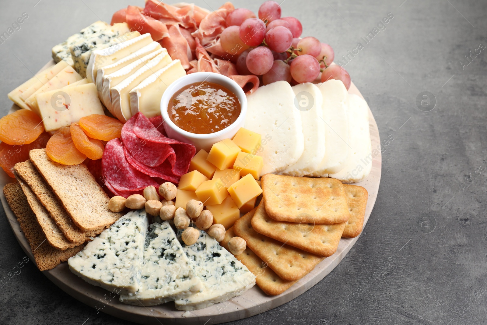 Photo of Different types of cut cheese and other snacks on grey textured table, closeup