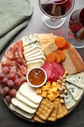 Photo of Different types of cut cheese and other snacks served with wine on grey textured table, flat lay