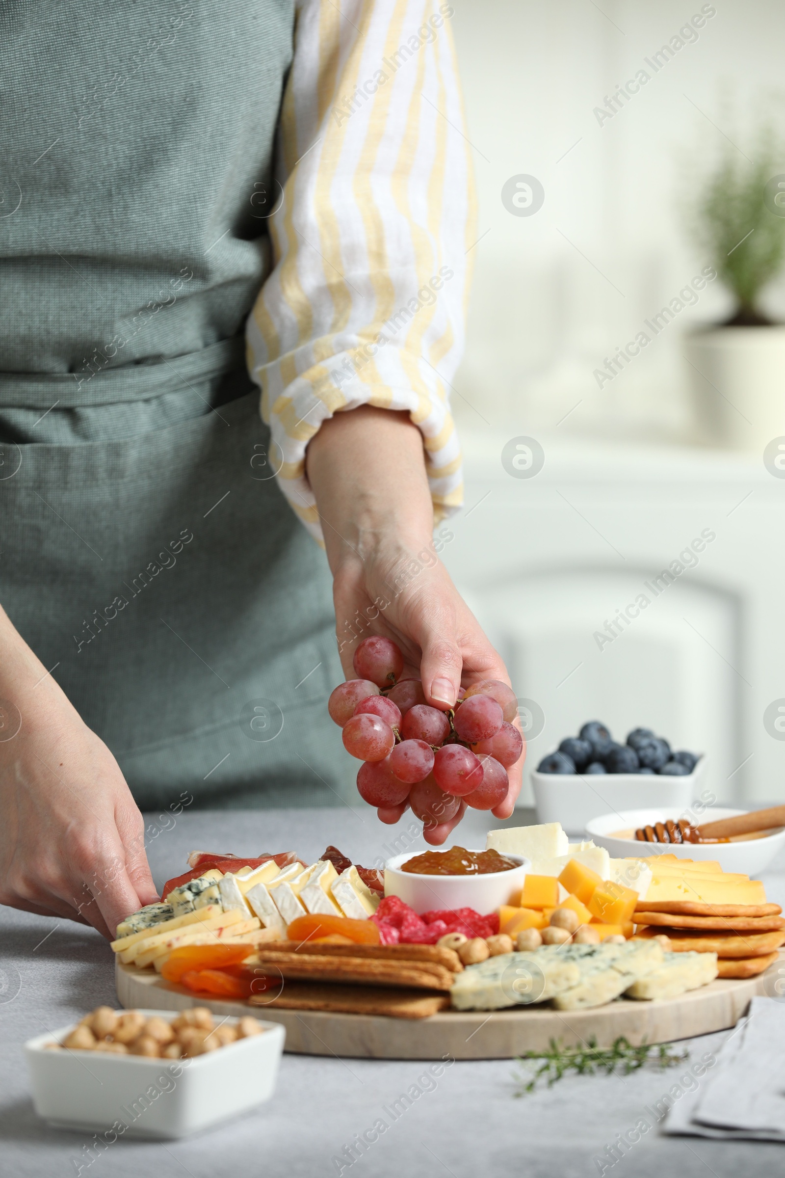 Photo of Woman serving antipasto platter with different types of cheese and other snacks with grapes at grey textured table indoors, closeup